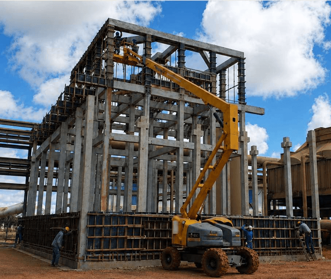 Montagem de estrutura industrial em concreto pré-moldado, com plataforma aérea e equipe em campo